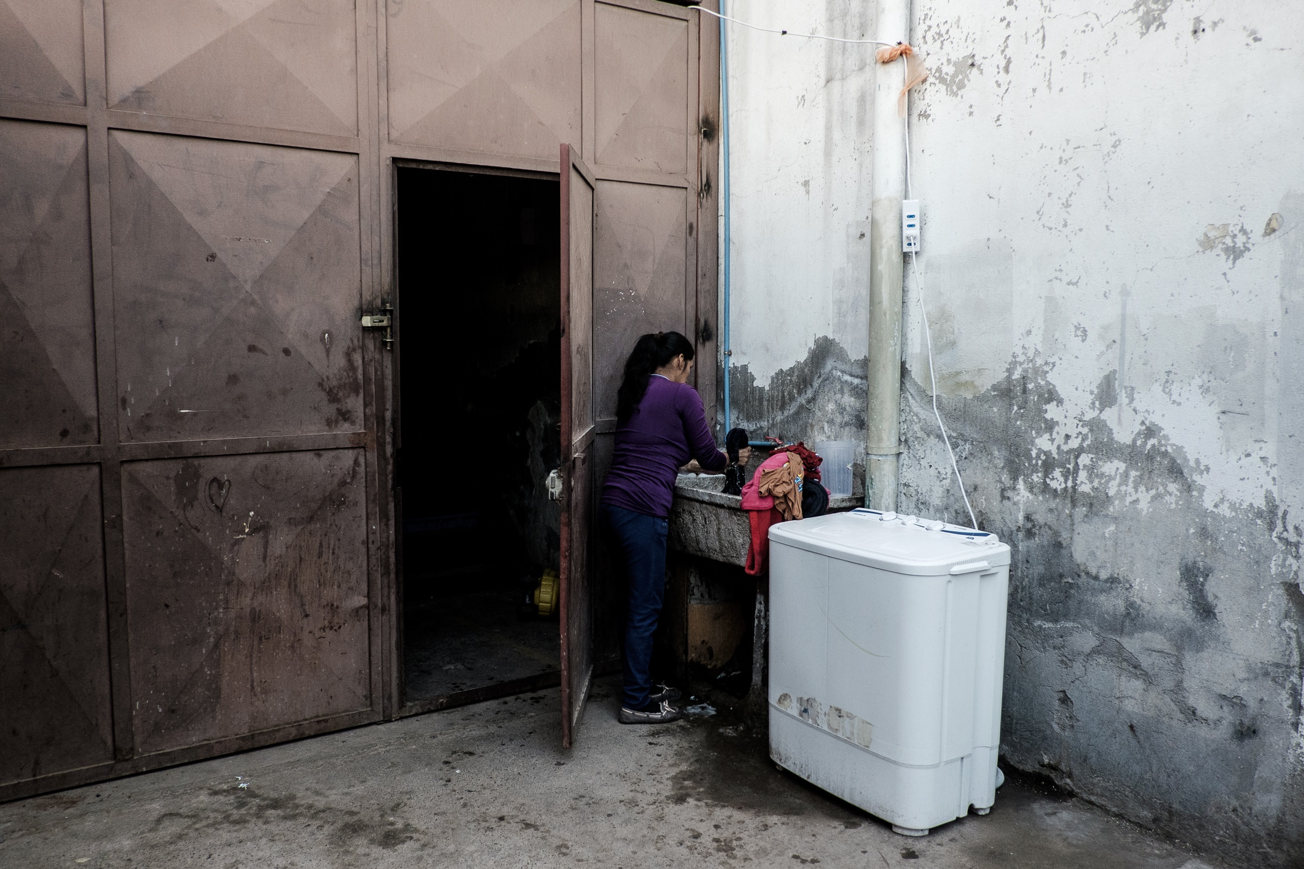 Una mujer, de origen peruano, lava su ropa en el único lugar con luz natural del galpón. Foto: Jorge Vargas | Migrar Photo