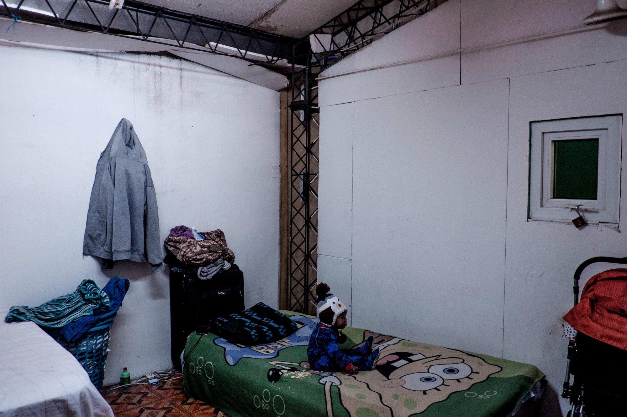 Un niño está sentado en una de las tres camas que hay en su habitación, que mide 12 metros cuadrado y que comparte con otras familias de origen haitiano | Foto: Jorge Vargas Migrar Photo